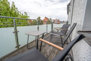 A balcony with a table and two chairs, a railing, and a view of buildings and trees.