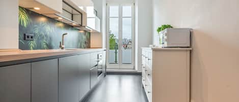 A modern kitchen with grey cabinets, a stainless steel countertop, and a view to the outside through a glass door.