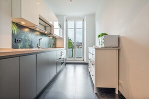 A modern kitchen with grey cabinets, a stainless steel countertop, and a view to the outside through a glass door.