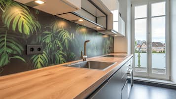 A modern kitchen with a wooden countertop, stainless steel sink, and a wall with a green leafy pattern.