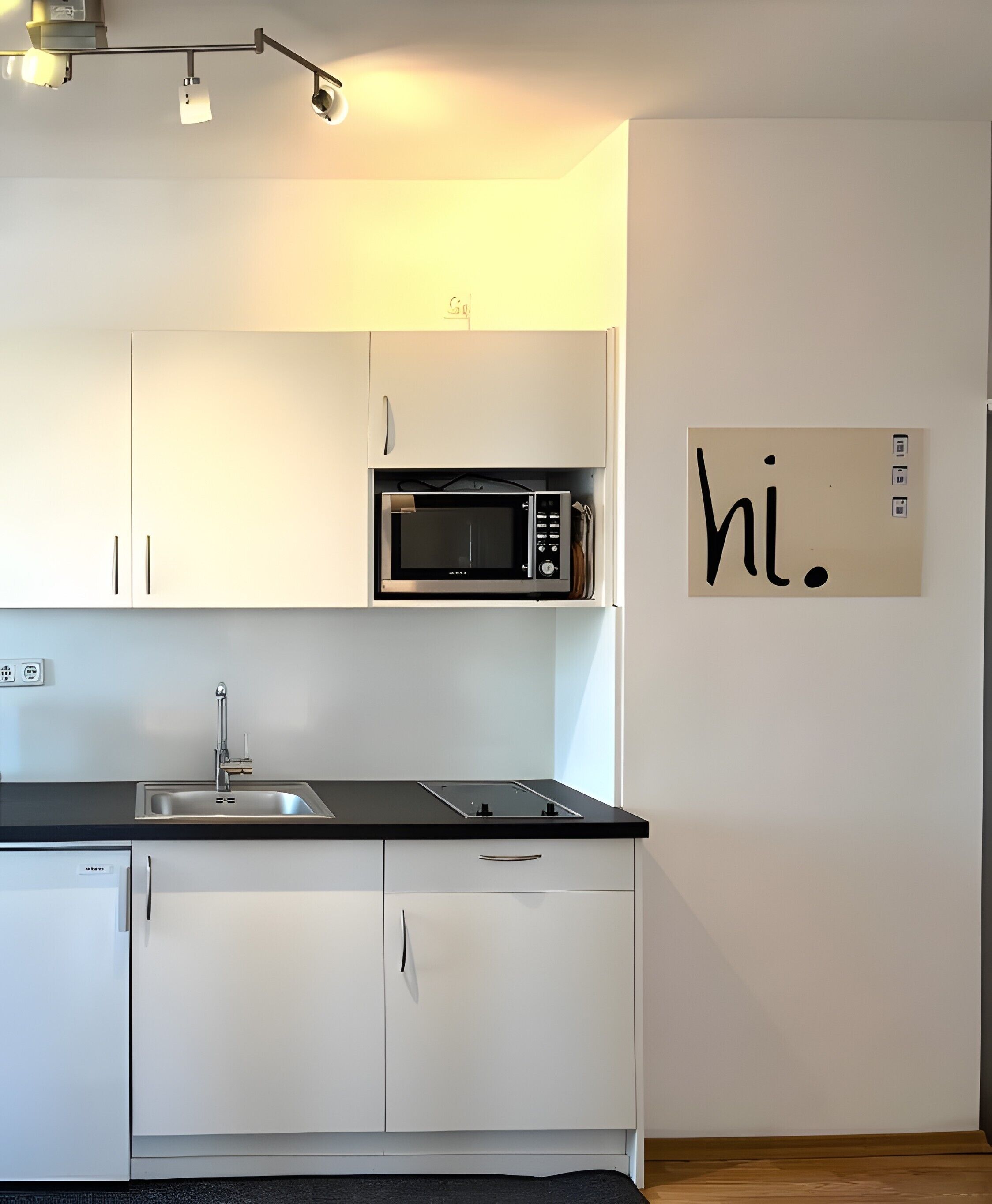 Una cocina moderna con gabinetes blancos, una encimera negra, un microondas, un fregadero y un letrero en la pared que dice 'hi'.