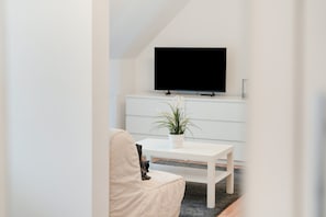 Una sala moderna con un sofá blanco, una mesita pequeña con una planta y un televisor de pantalla plana montado en un mueble blanco.