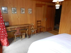 A room with a bed, a desk, two chairs, a lamp, and a door. - Tree-Tops, Chalet Appartement/Fewo, Dusche und Bad, WC 9-Bettwohnung by Interhome (Gstaad)