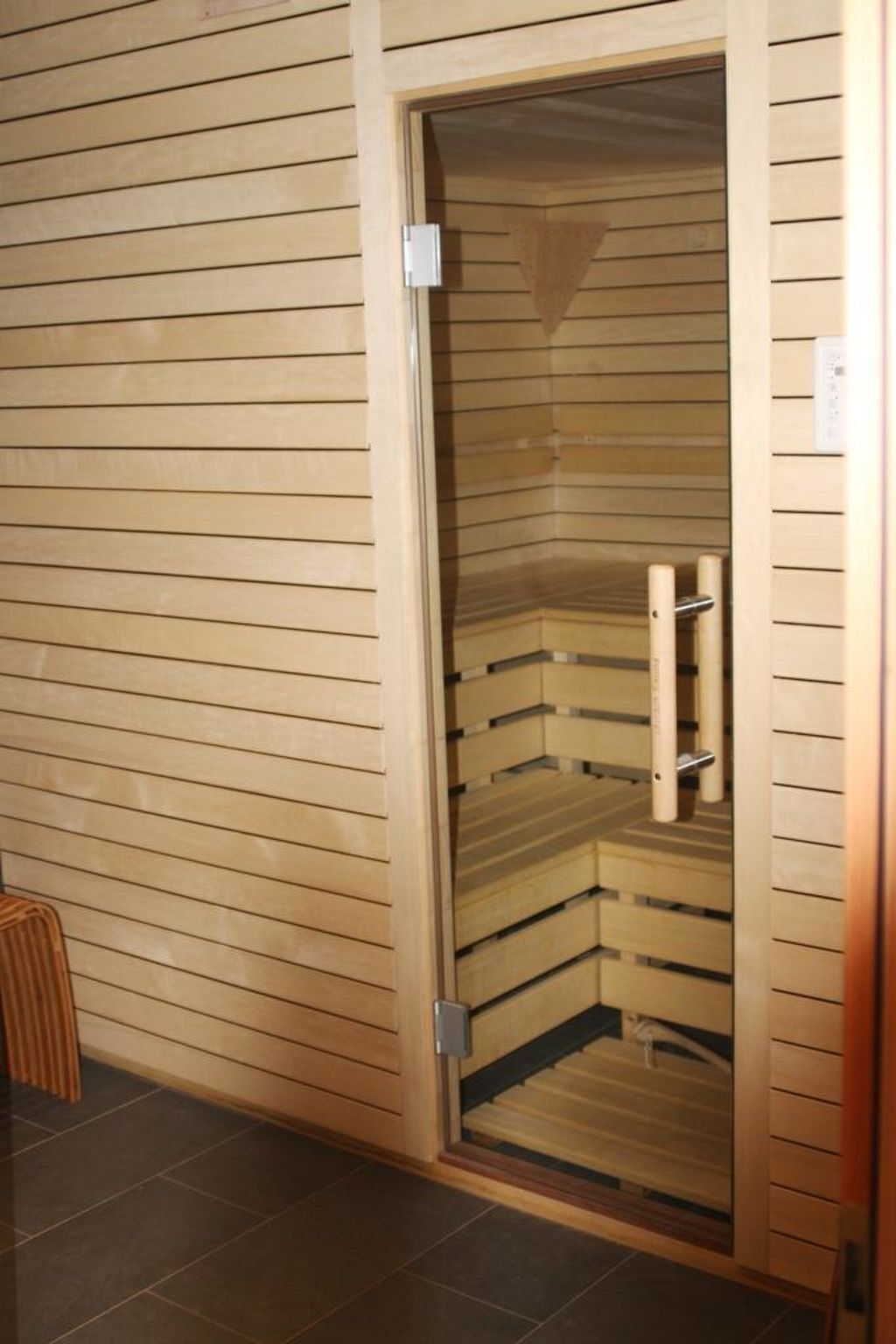 Un sauna avec une structure extérieure en bois et une porte en verre, comprenant un banc et un porte-serviettes à l’intérieur.