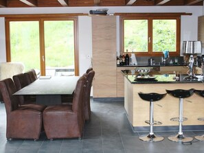 A modern kitchen with a dining area, featuring a large table, bar stools, and a view of greenery through the windows. - Nubes, Chalet Appartement/Fewo, Dusche oder Bad, WC 12-Bettwohnung by Interhome (Zweisimmen)