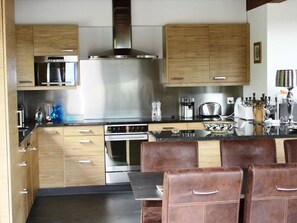 Una cocina moderna con armarios de madera, extractor de acero inoxidable y un comedor con sillas de cuero.