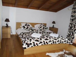 A bedroom with a wooden bed, two bedside tables with lamps, a cow print bedspread, and a fur rug on the floor. - Nubes, Chalet Appartement/Fewo, Dusche oder Bad, WC 12-Bettwohnung by Interhome (Zweisimmen)