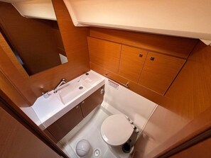 A compact bathroom with a white sink, toilet, and wooden cabinetry. - Sun-Kissed Sailing Adventure in Istria, Croatia (Pula)