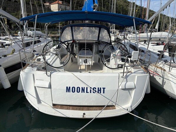 A sailboat named 'MOONLIGHT' docked at a marina with other boats, a blue canopy, and a stone building in the background. - Sun-Kissed Sailing Adventure in Istria, Croatia (Pula)