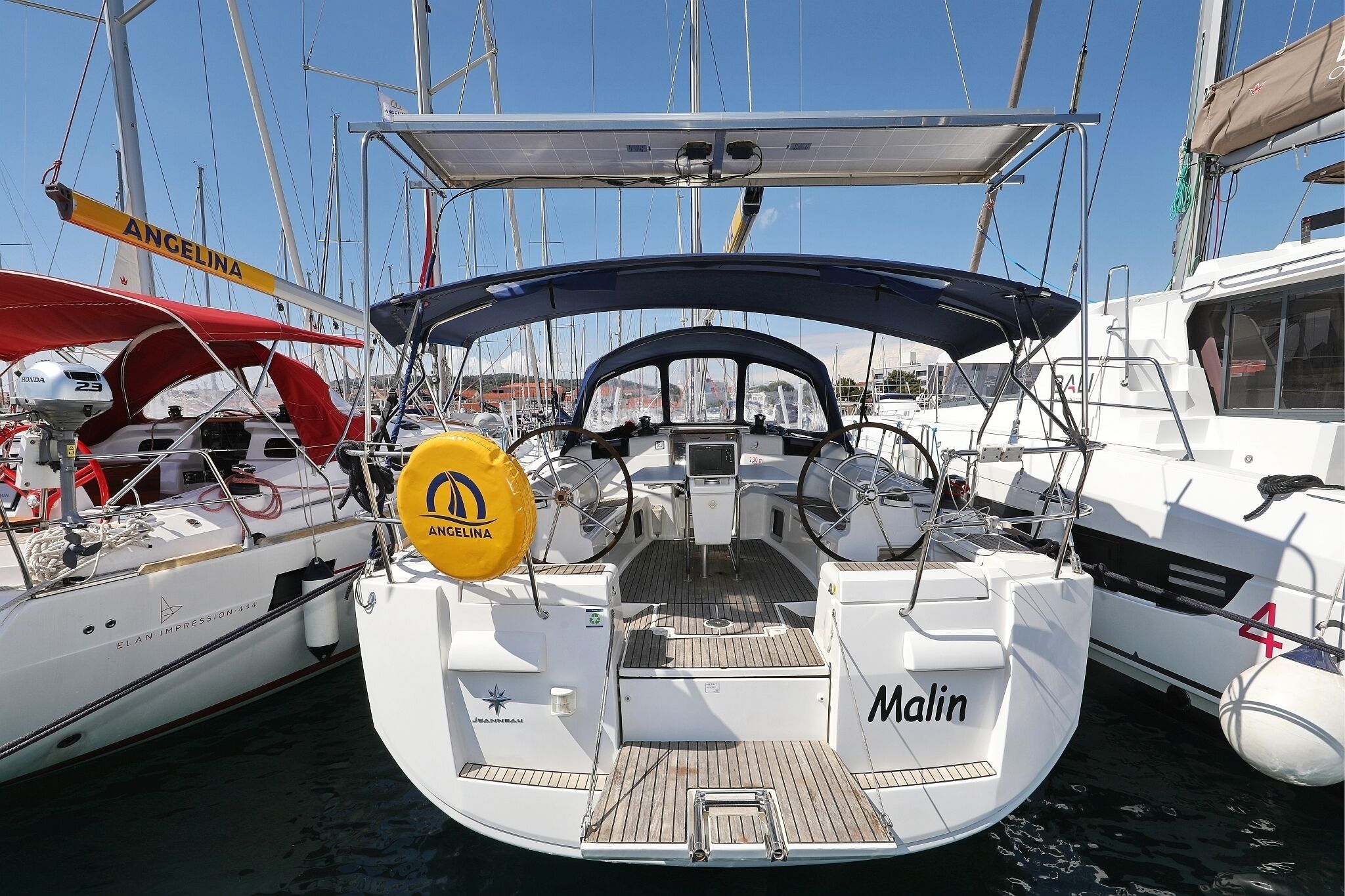 Un velero llamado 'Malin' atracado en un puerto deportivo, con otros barcos, un timón y un cabestrante a la vista.