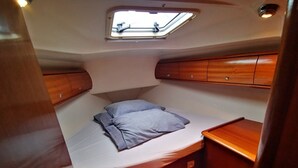 Une petite cabine comprenant un lit, une petite table, un puits de lumière et des meubles en bois.