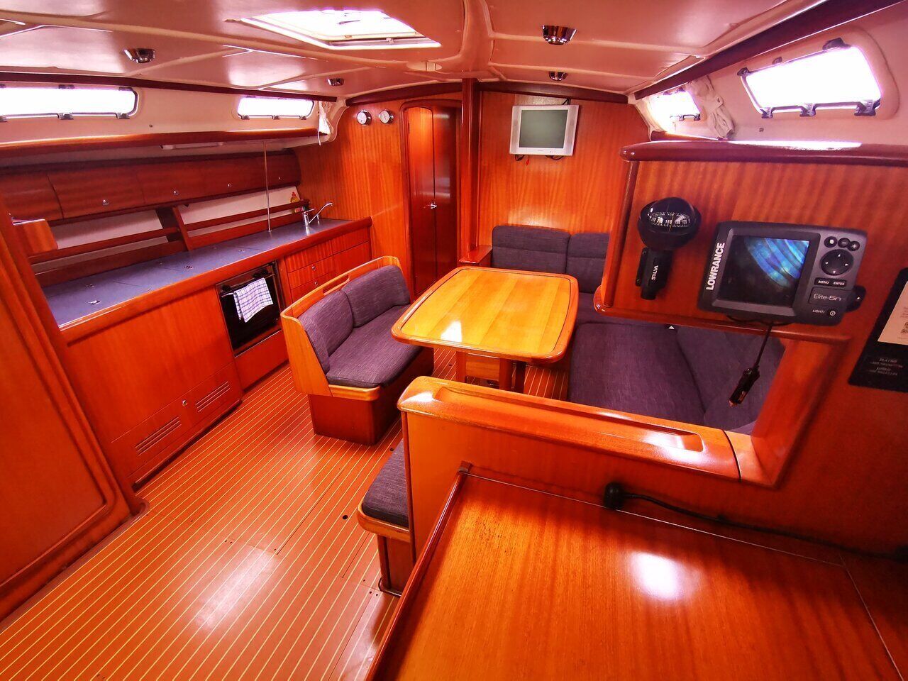 A compact boat interior with a dining area, seating, a small kitchen, and a television.