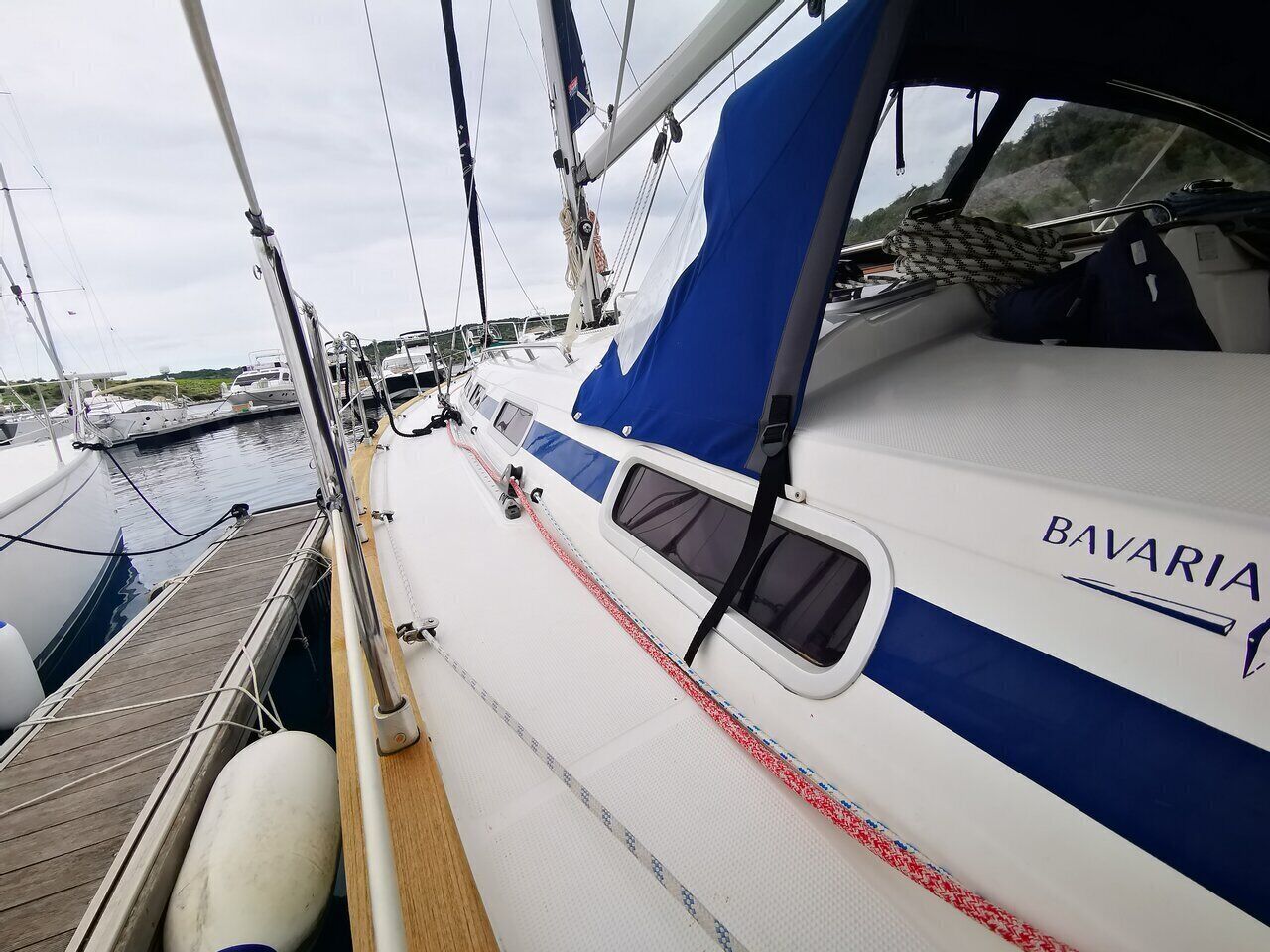 A sailboat docked at a marina with a blue and white color scheme, a name 'BAVARIA' on the side, and a wooden deck.