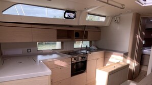 Een kleine keuken met een fornuis, oven en spoelbak, houten kastjes en een klein raam.