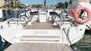 Boot genaamd MARACUYA afgemeerd in een jachthaven met een houten dek, stuurrad en reddingsboei.