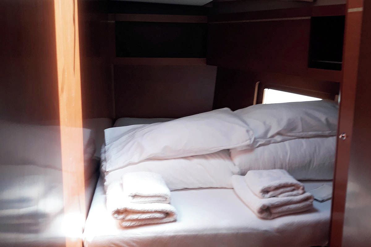 A small, single-bed room with a wooden headboard, a window, and a television mounted on the wall.