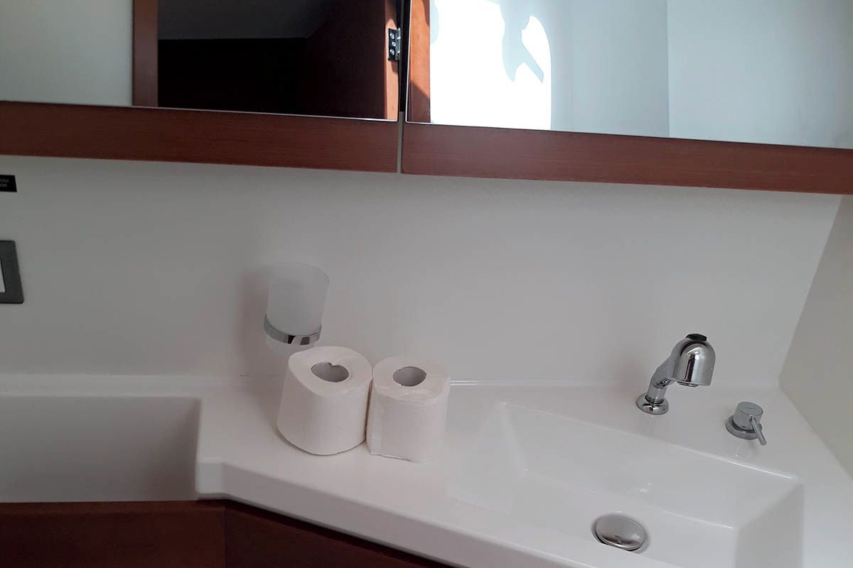 Um banheiro com pia branca, dois rolos de papel higiênico, uma torneira e um espelho sobre a pia.