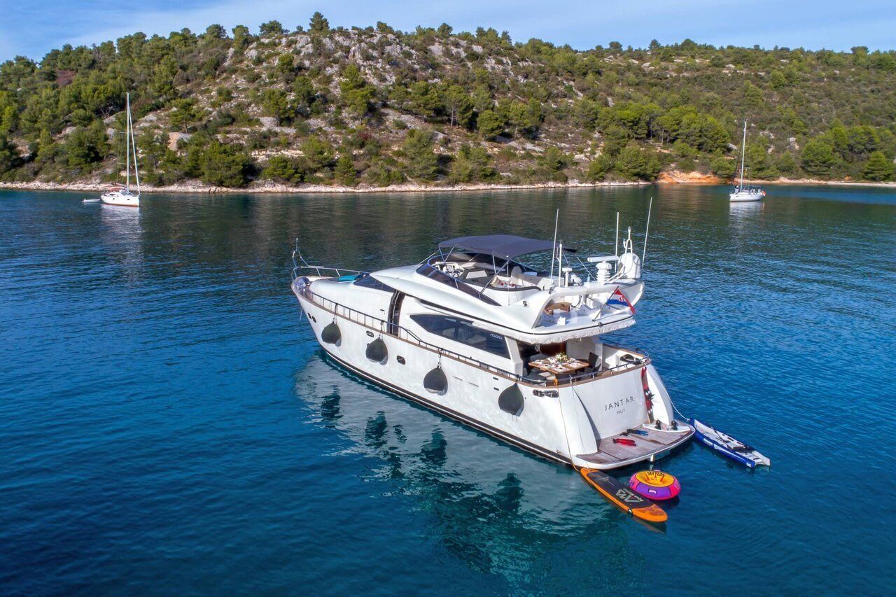 A large yacht docked at a marina with a forested hill in the background.
