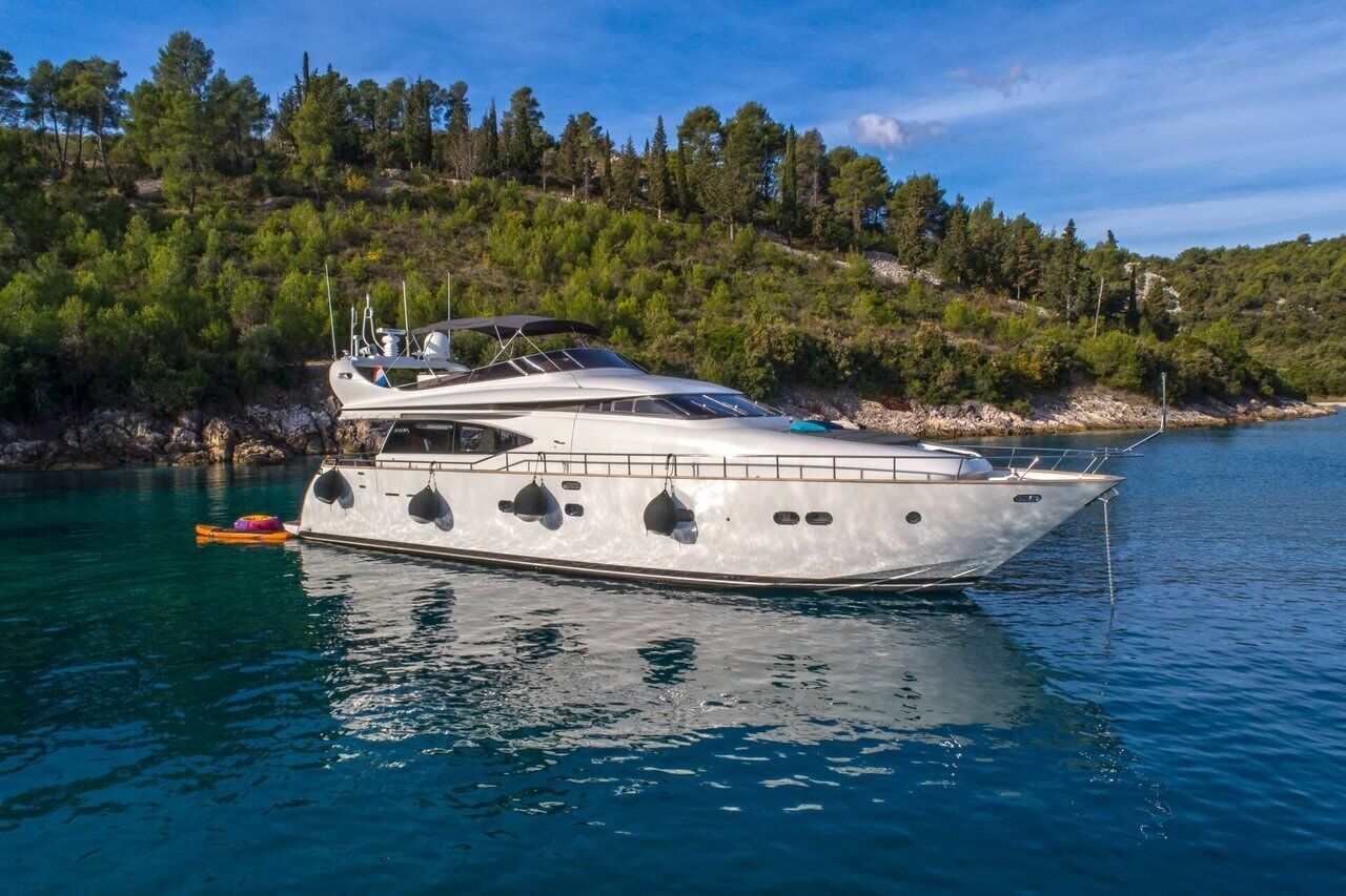 En lyxyacht låg förtöjd vid ett lugnt vattenområde, med en skogbeklädd sluttning i bakgrunden.