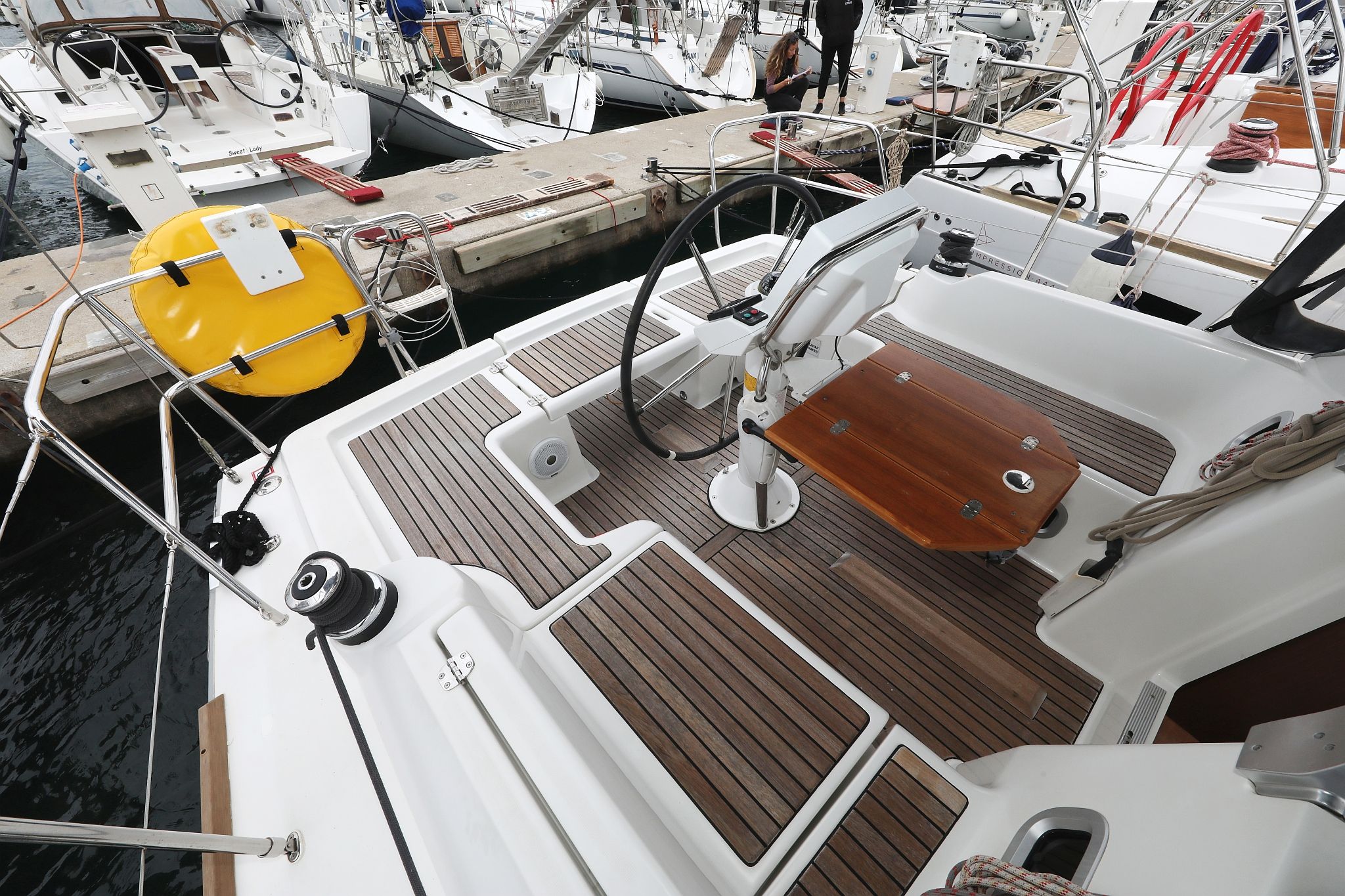 Cubierta de barco con timón, salvavidas amarillo y piso de madera.