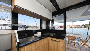 A modern kitchen with a view of the marina, wooden cabinets, a black countertop, and a dining area with a table and chairs. - Sun-Kissed Sailing Adventure in Zadar, Croatia (Biograd na moru)