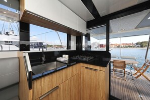 A modern kitchen with a view of the marina, wooden cabinets, a black countertop, and a dining area with a table and chairs. - Sun-Kissed Sailing Adventure in Zadar, Croatia (Biograd na moru)