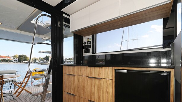 A modern kitchen with wooden cabinets, a black refrigerator, and a window overlooking a marina. - Sun-Kissed Sailing Adventure in Zadar, Croatia (Biograd na moru)
