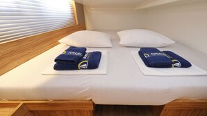 A bed with white bedding, two pillows, and two folded towels with a logo. - Sun-Kissed Sailing Adventure in Zadar, Croatia (Biograd na moru)