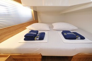 A bed with white bedding, two pillows, and two folded towels with a logo. - Sun-Kissed Sailing Adventure in Zadar, Croatia (Biograd na moru)