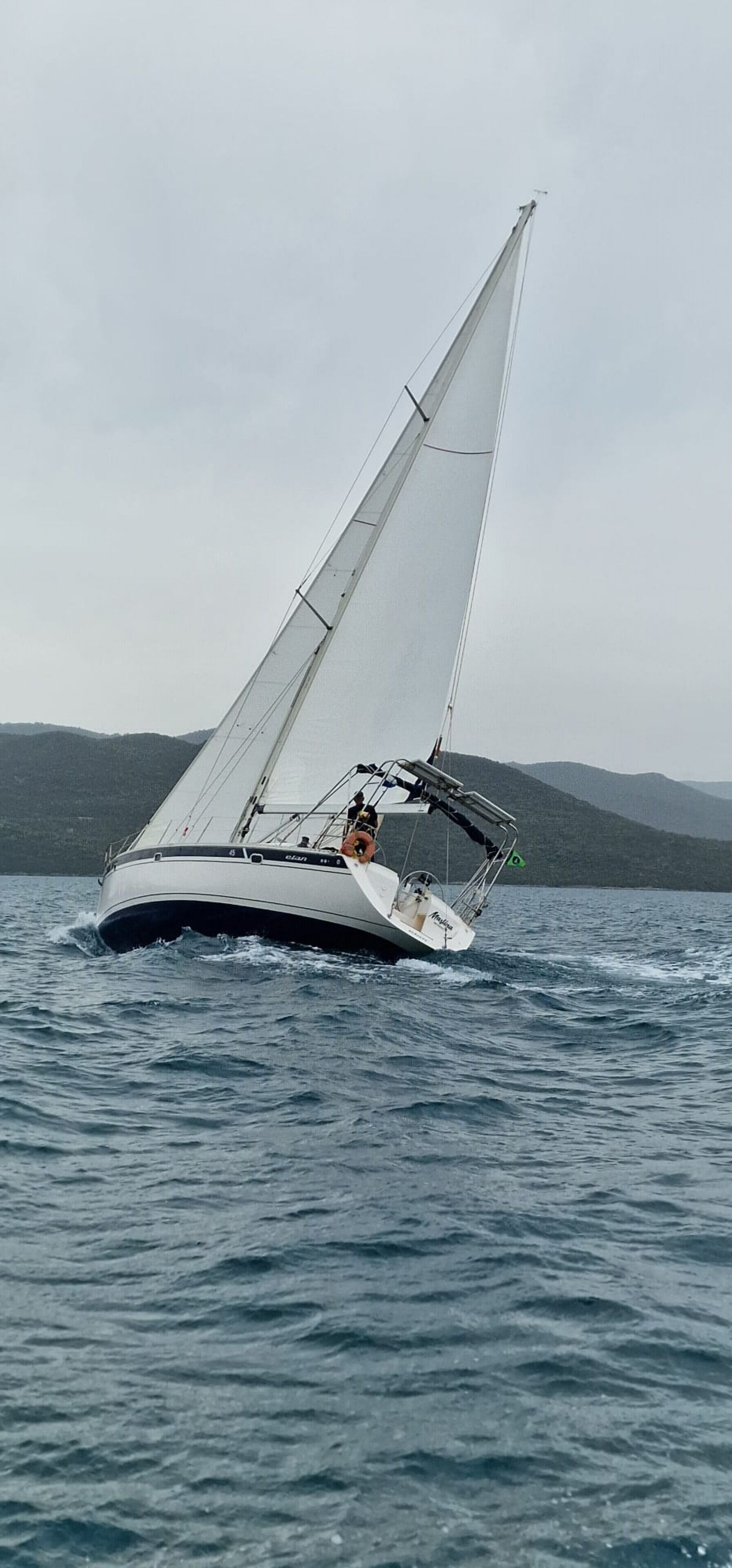 A sailboat on water with a mountainous landscape in the background.