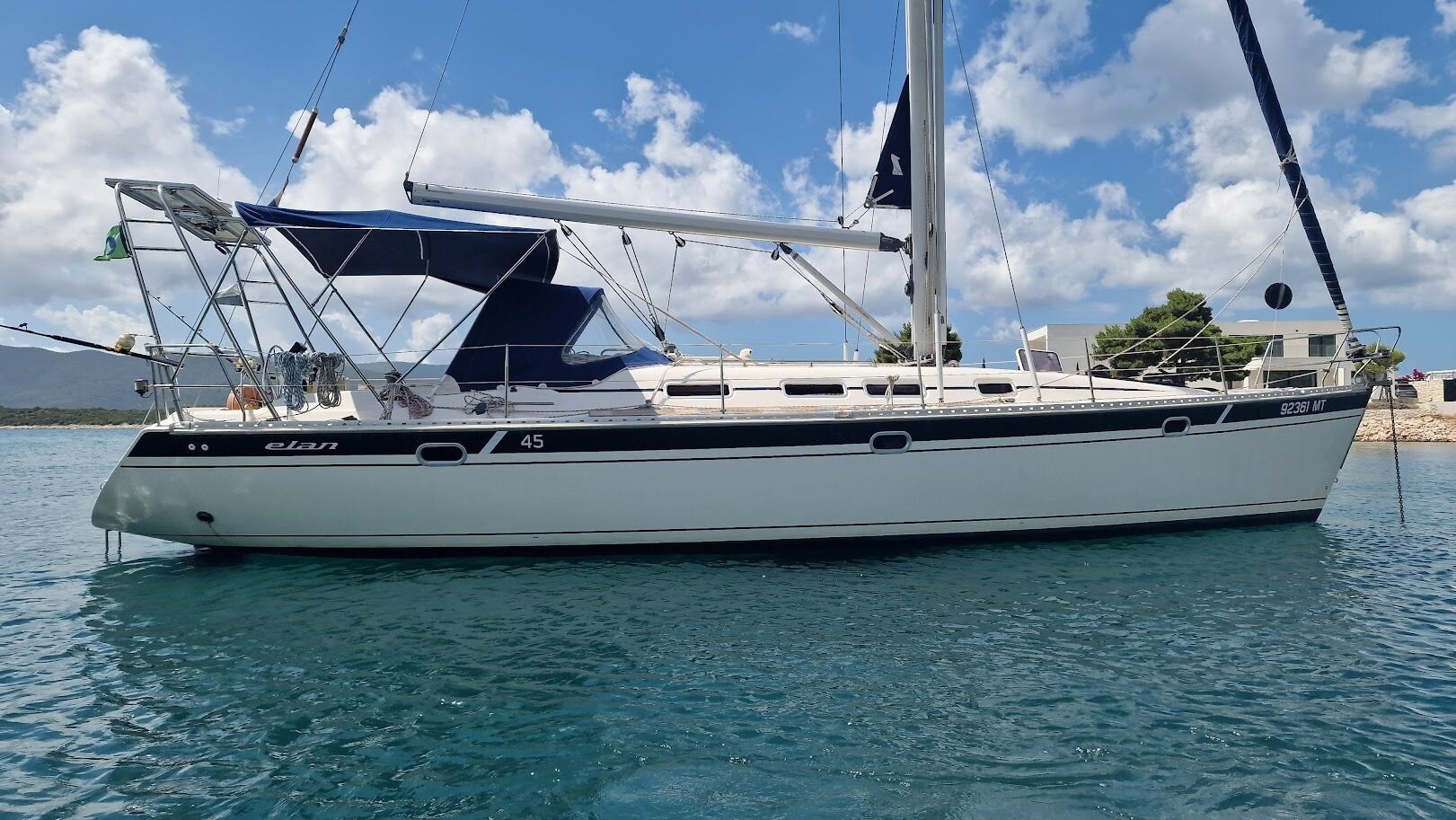 A sailboat named 'elan' docked at a marina with clear skies and calm waters.