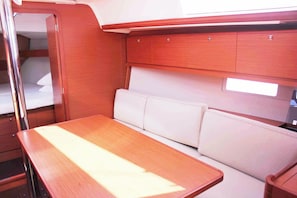 A compact cabin with a wooden table, a bench with cushions, and a small bed. - Sun-Kissed Sailing Adventure in Islas Sarónicas (Alimos)
