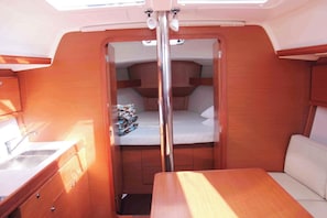 A compact interior with a wooden bench, a small table, a sink, and a bed with a mattress and pillows. - Sun-Kissed Sailing Adventure in Islas Sarónicas (Alimos)