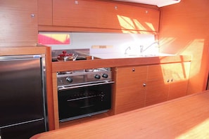 A compact kitchen with a refrigerator, stove, oven, and sink. - Sun-Kissed Sailing Adventure in Islas Sarónicas (Alimos)