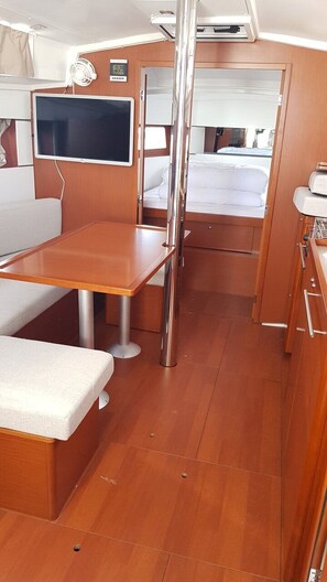 A compact cabin with a wooden table, a bench, a bed, a TV, and a small kitchenette.