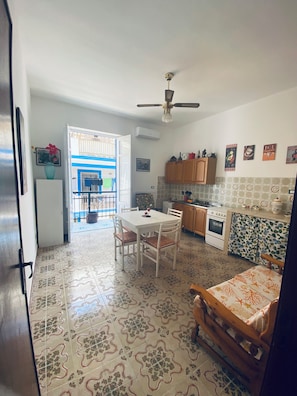 Une cuisine avec une table à manger, des chaises, un ventilateur de plafond et un sol carrelé.