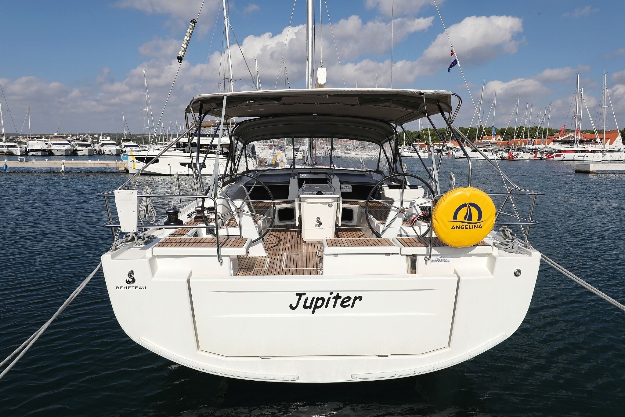 A sailboat named 'Jupiter' docked at a marina with other boats and a clear sky.