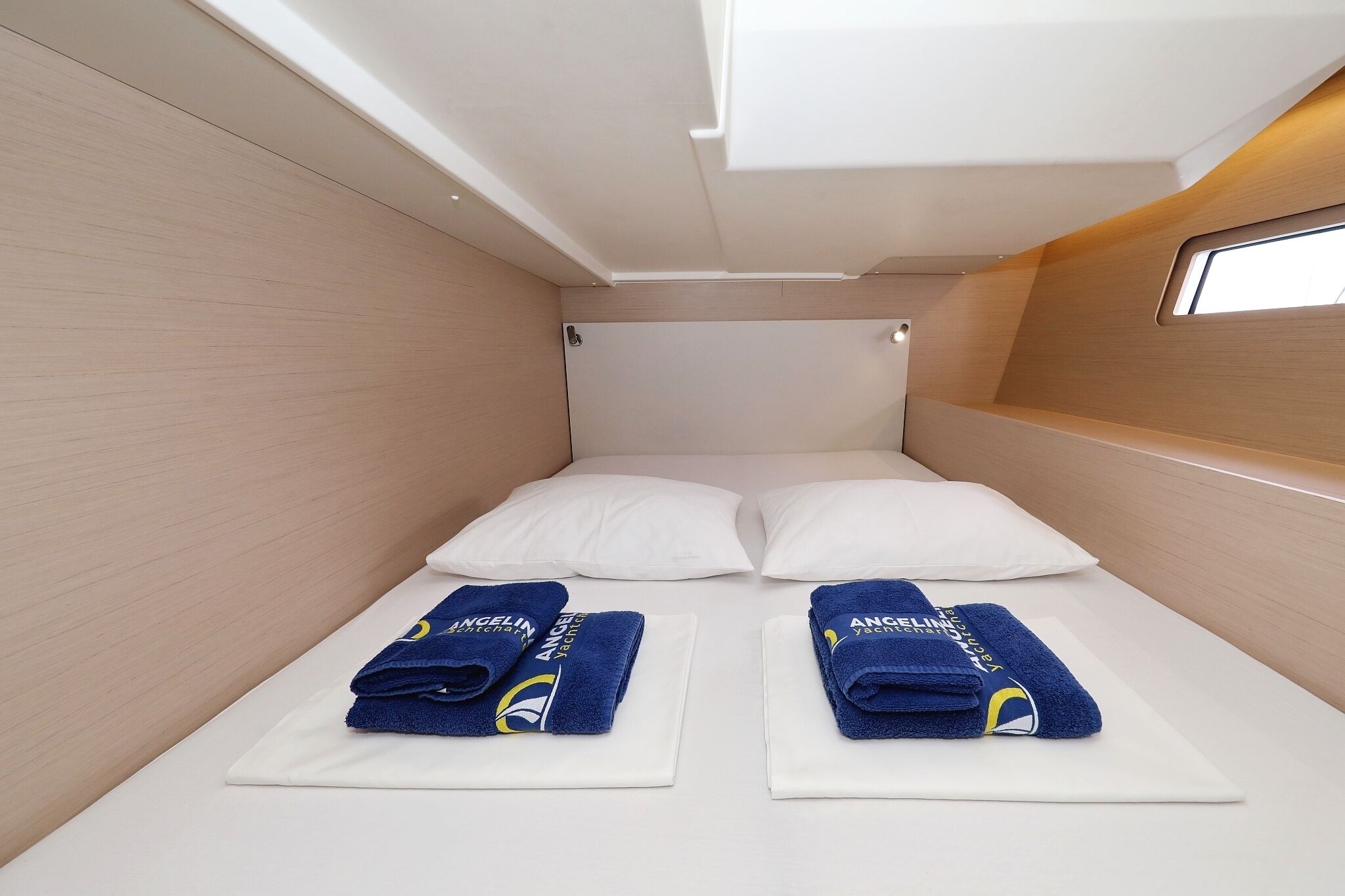 A small, modern room with a bed, two pillows, and two towels on white bedsheets.