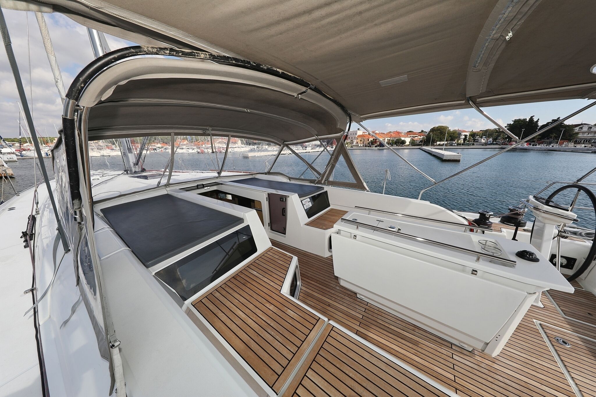 Ein Bootsdeck mit überdachter Sitzgruppe, Steuer und Blick auf den Hafen.