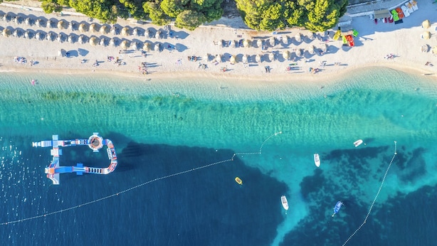 Vista aérea de una playa con aguas turquesas cristalinas, un muelle y varios barcos.