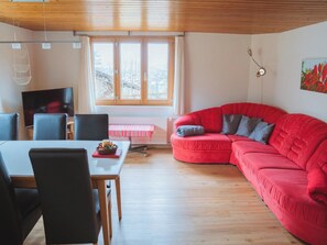 A modern living room with a red sofa, a dining table with chairs, a TV, and a window with curtains. - Burkhalter Appartement/Fewo, Dusche oder Bad, WC 4-Bettwohnung by Interhome (Zweisimmen)
