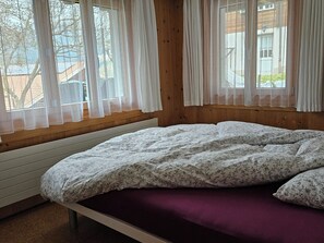 A bedroom with a bed, wooden walls, and windows with sheer curtains. - Burkhalter Appartement/Fewo, Dusche oder Bad, WC 4-Bettwohnung by Interhome (Zweisimmen)
