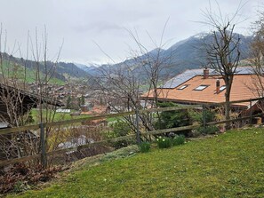 A rural landscape with a house featuring a tiled roof, a wooden fence, and a view of distant mountains. - Burkhalter Appartement/Fewo, Dusche oder Bad, WC 4-Bettwohnung by Interhome (Zweisimmen)