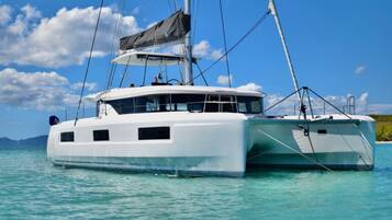 Een witte catamaran met een kajuit, zeilen en een helderblauwe lucht op de achtergrond.