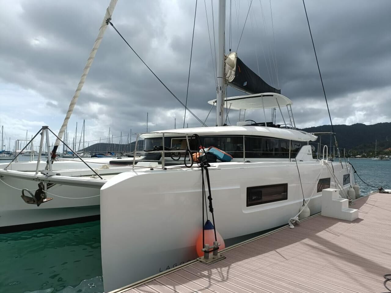 Eine weiße Yacht liegt in einer Marina vor blauem Himmel und Bergen im Hintergrund.