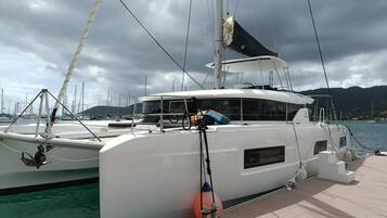 Eine weiße Yacht liegt in einer Marina vor blauem Himmel und Bergen im Hintergrund.