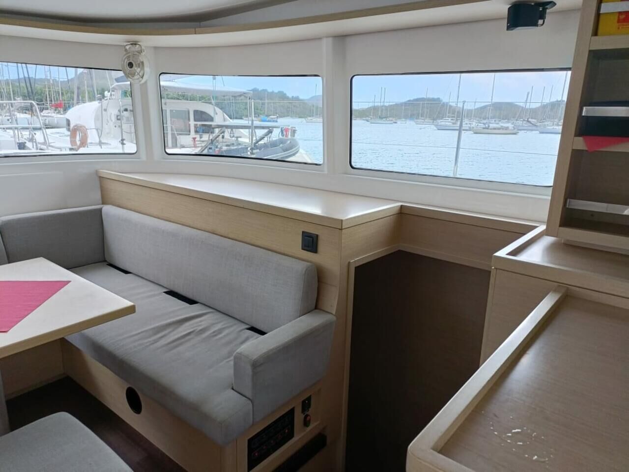 A cabin with a cushioned seating area, a small table, and windows offering a view of the marina.