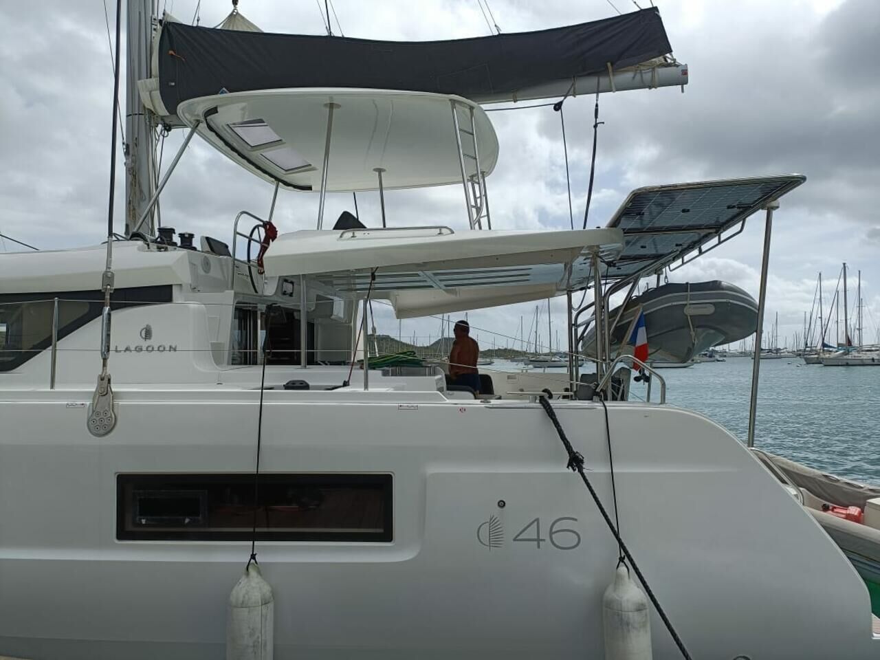 A sailboat with a cabin, a person seated, and a marina in the background.