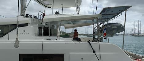 A sailboat with a cabin, a person seated, and a marina in the background.