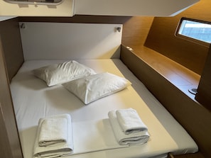 Ein kleines Bett mit Kissen und gefalteten Handtüchern, ein Fenster und ein Tisch mit einer Lampe.